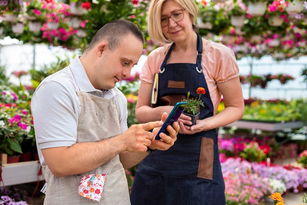 Man with Down syndrome happily engaging in creative work at a cluttered table filled with various art supplies, in a room with shelves of colorful items.